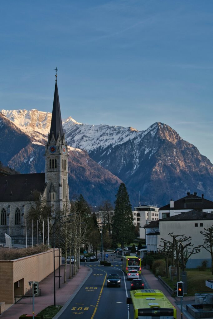 Scenic view of the Vaduz church steeple against the Alpine mountains at sunset.